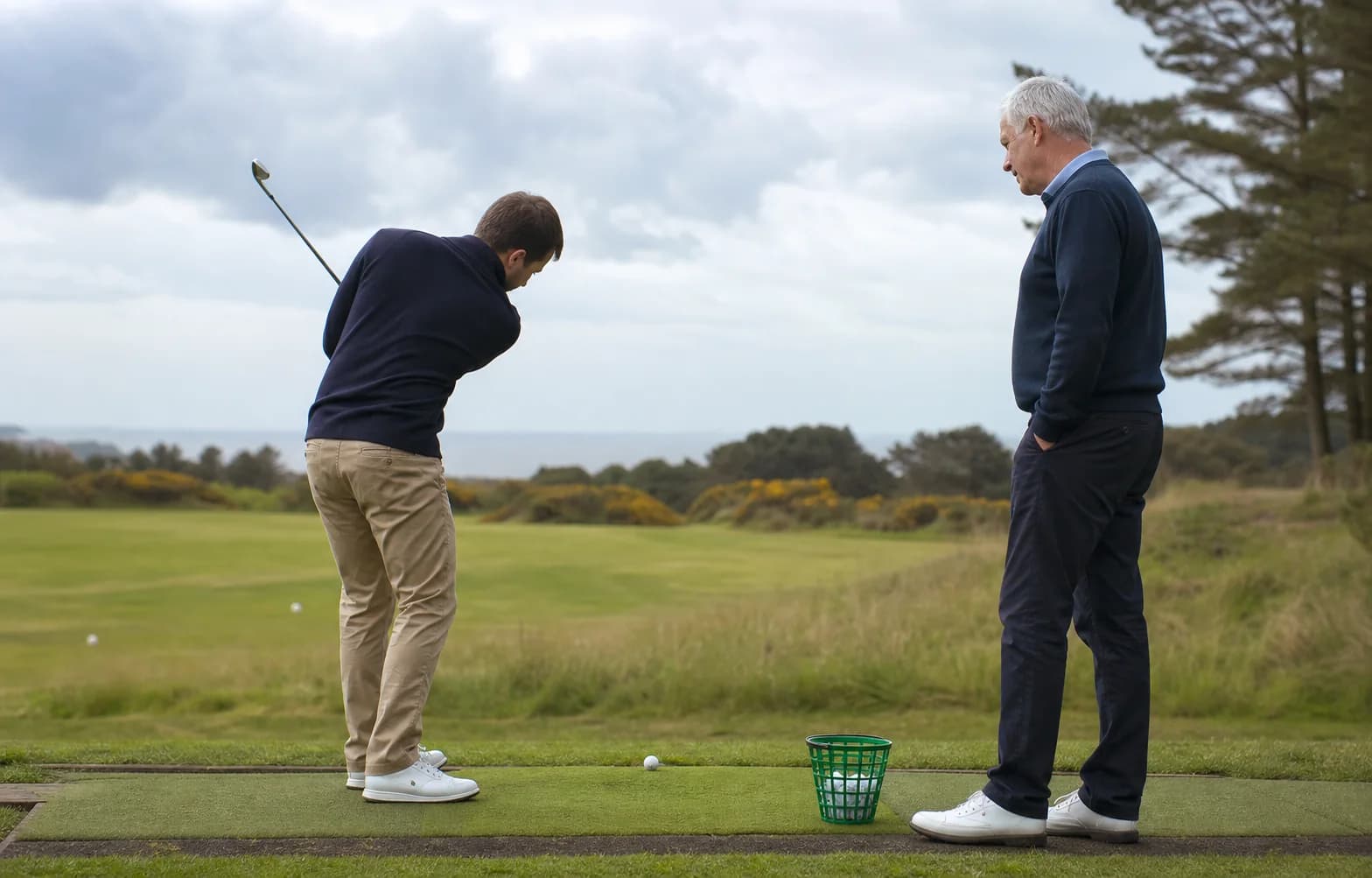 An adult beginner making a small golf swing while a coach observes