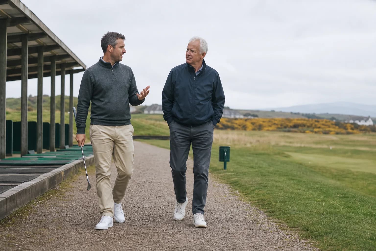 An adult golfer and an older coach talking beside a local practice ground